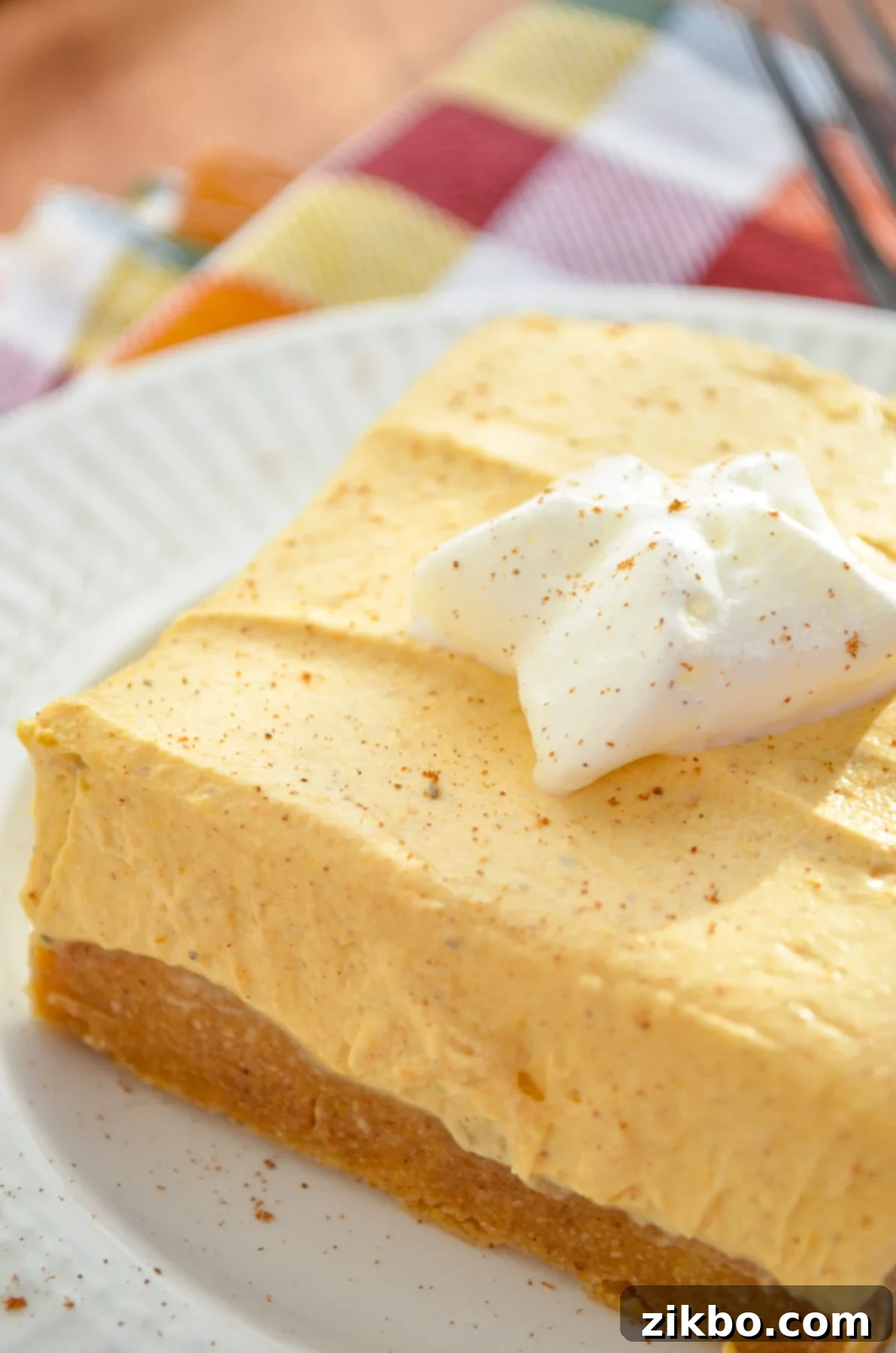 A single no bake pumpkin cheesecake bar, served with a dollop of whipped cream and a sprinkle of cinnamon on top.