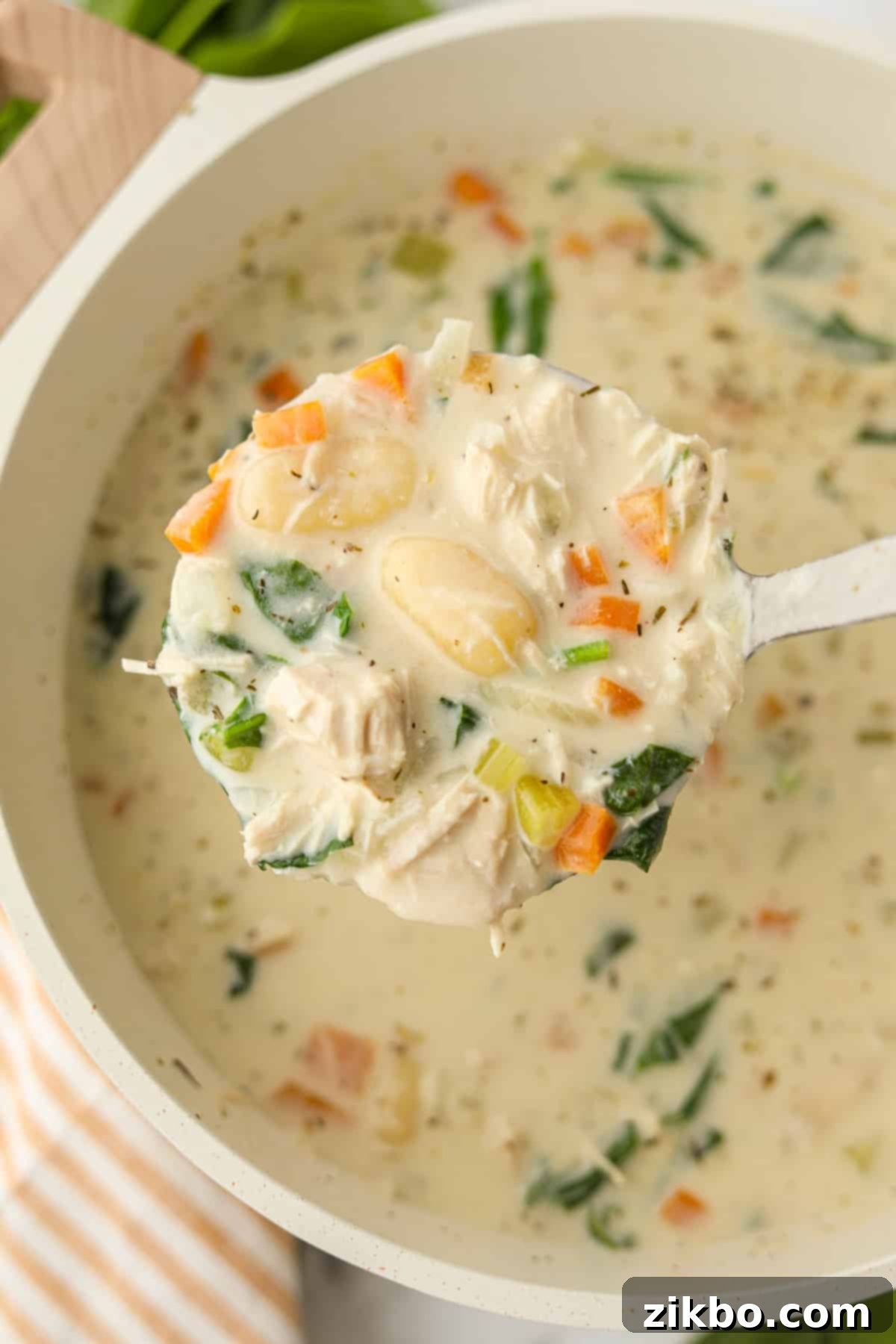A ladle holding up a scoop of creamy turkey and gnocchi soup, highlighting the tender gnocchi and turkey pieces.