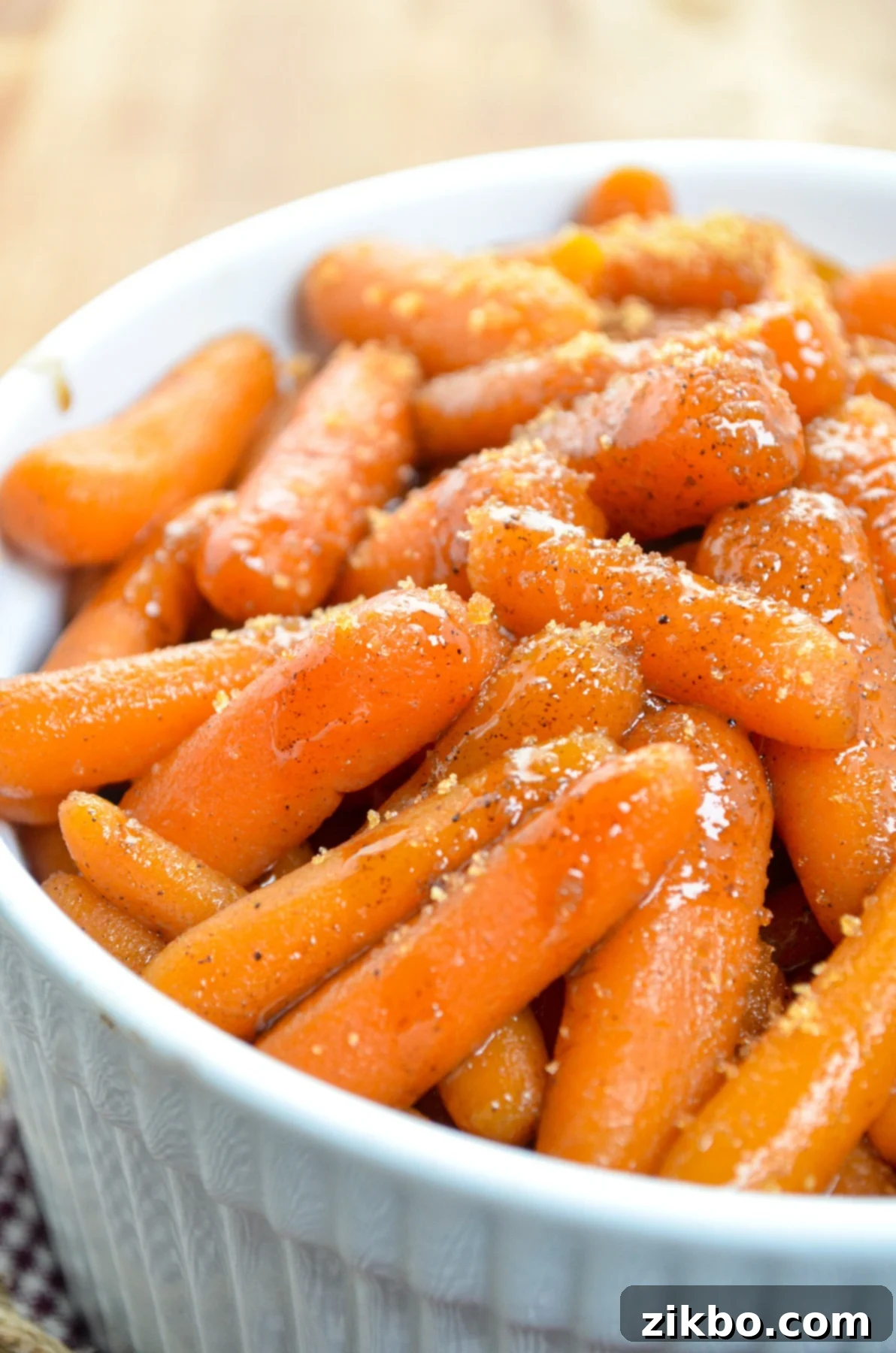 A white serving dish, filled with slow cooker maple carrots. Sprinkled with additional brown sugar.