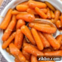 A bowl of maple glazed carrots, with a large serving spoon taking a portion out.
