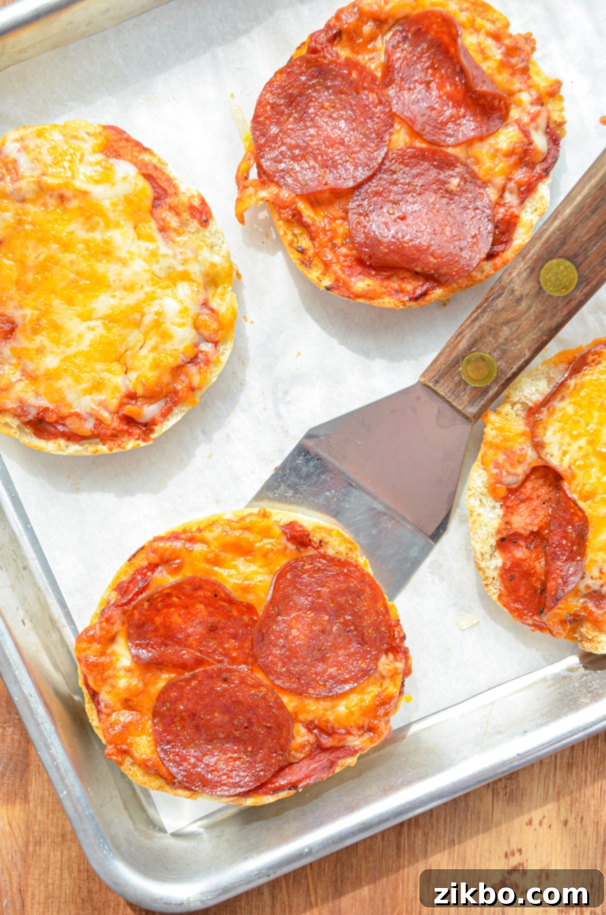 English muffin pizzas being lifted with a spatula.