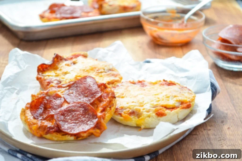A plate of english muffin pizzas, with a prepared baking sheet full in the background.