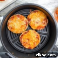 An air fryer with english muffin pizzas in the basket.