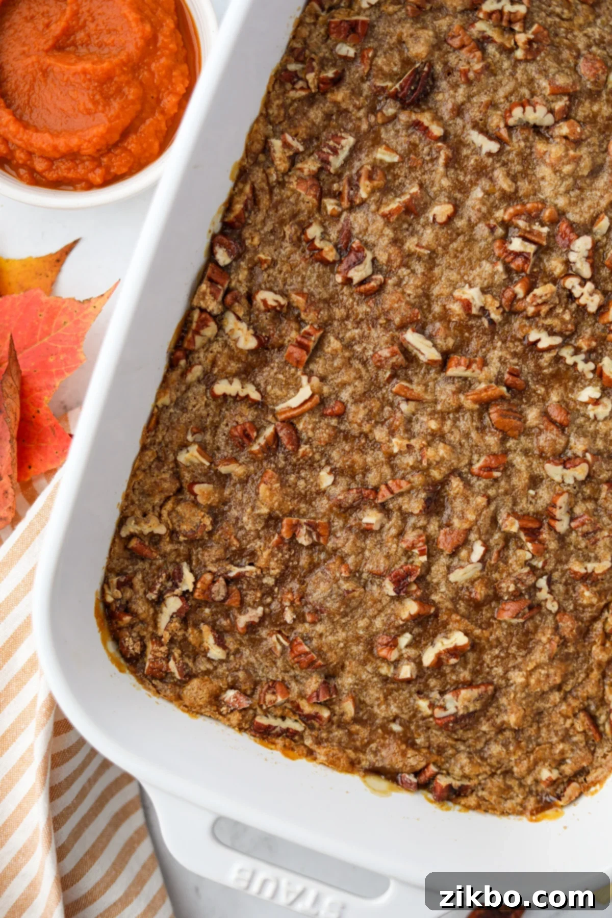 A white baking dish filled with a casserole topped with pecans and brown sugar, ready for serving.