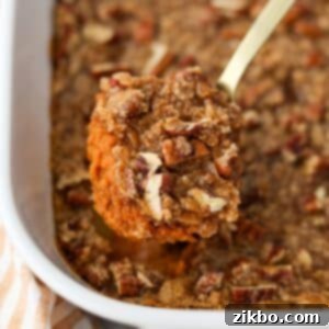 A spoon taking a portion of pumpkin casserole topped with pecans.