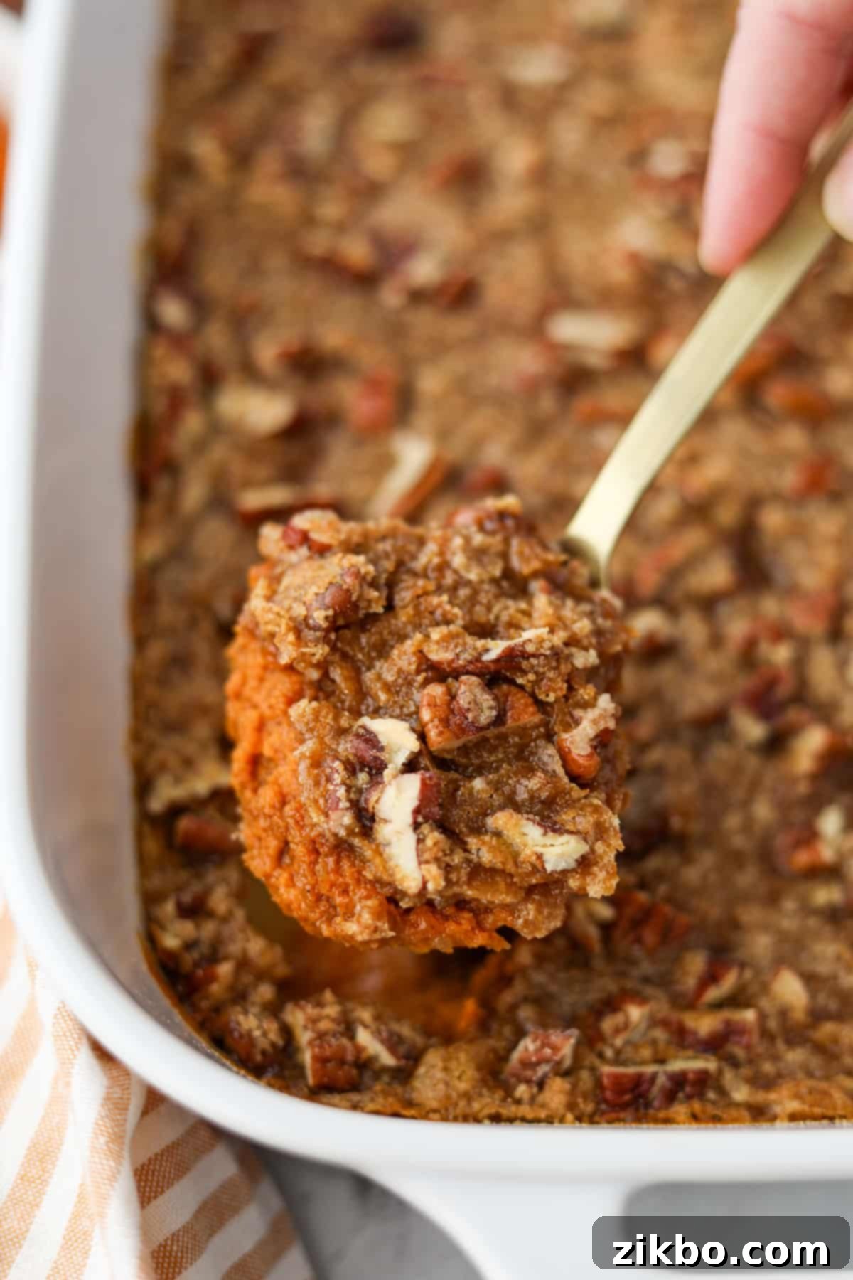 Scooping a warm, creamy portion of pumpkin casserole topped with crunchy pecans from a baking dish.