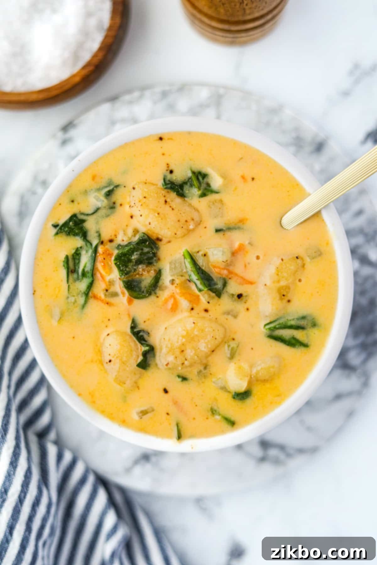 A white bowl filled with creamy cheesy gnocchi soup, adorned with spinach and shredded carrots.