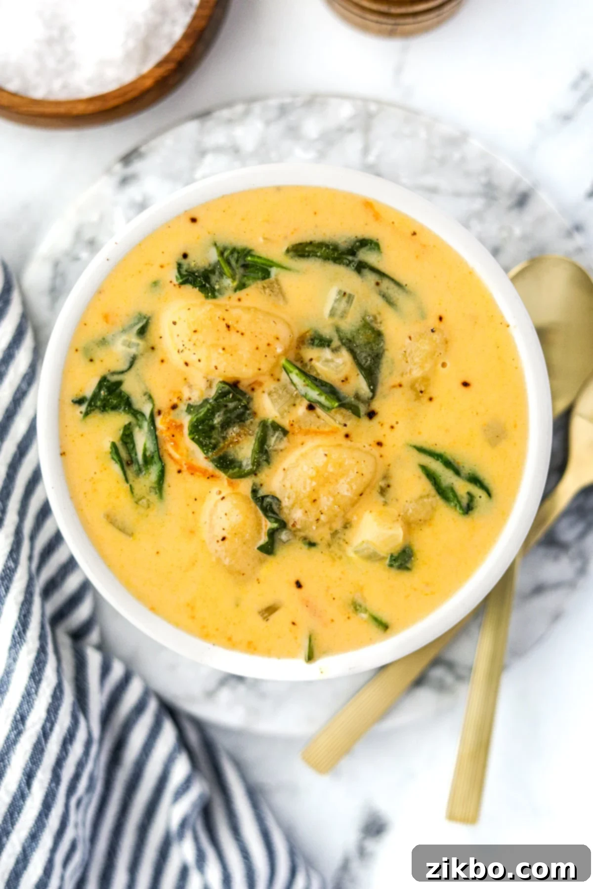 An overhead view of a steaming bowl of cheesy gnocchi soup, garnished with spinach.