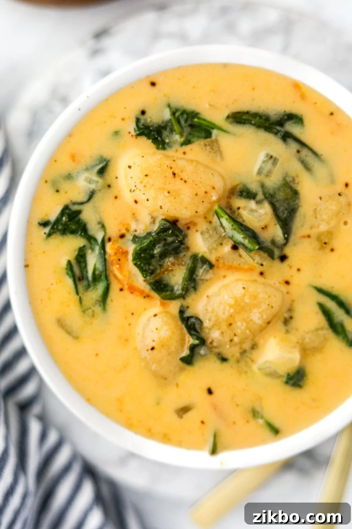 A white bowl filled with cheesy gnocchi soup, showing the texture of the gnocchi, carrots, and wilted spinach.