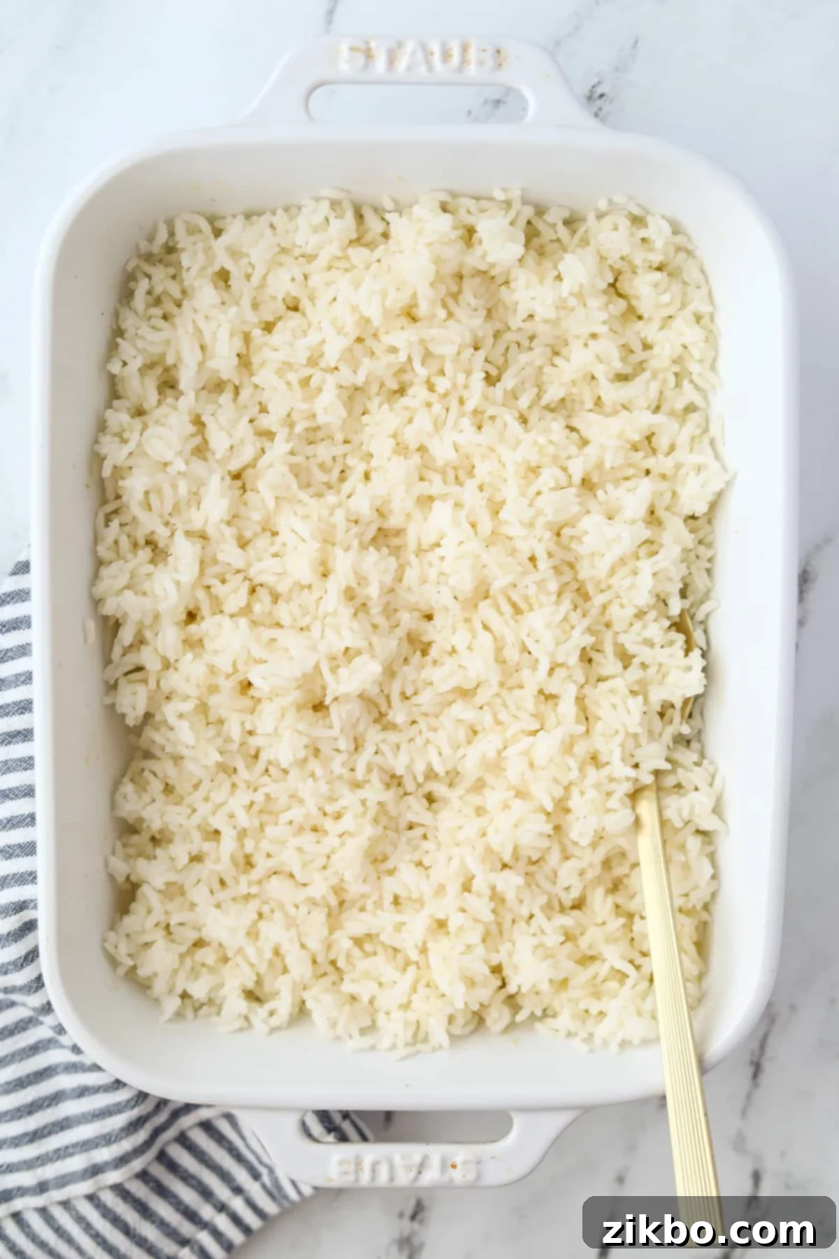 Golden Baked Rice 5 A baking dish filled with perfectly cooked, fluffy white rice, with a serving spoon poised to scoop a portion, showcasing its ideal texture.