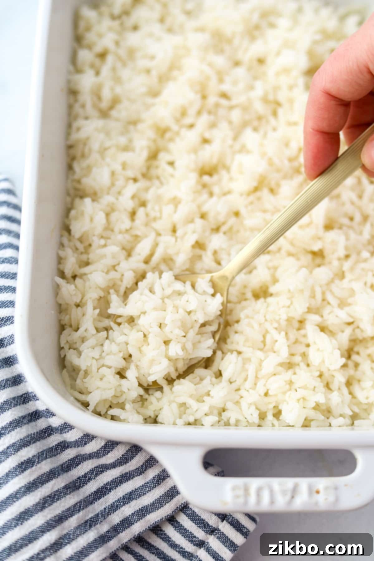 Golden Baked Rice 7 A hand holding a serving spoon, scooping a generous portion of hot, fluffy cooked rice from a casserole dish, emphasizing its perfect texture.