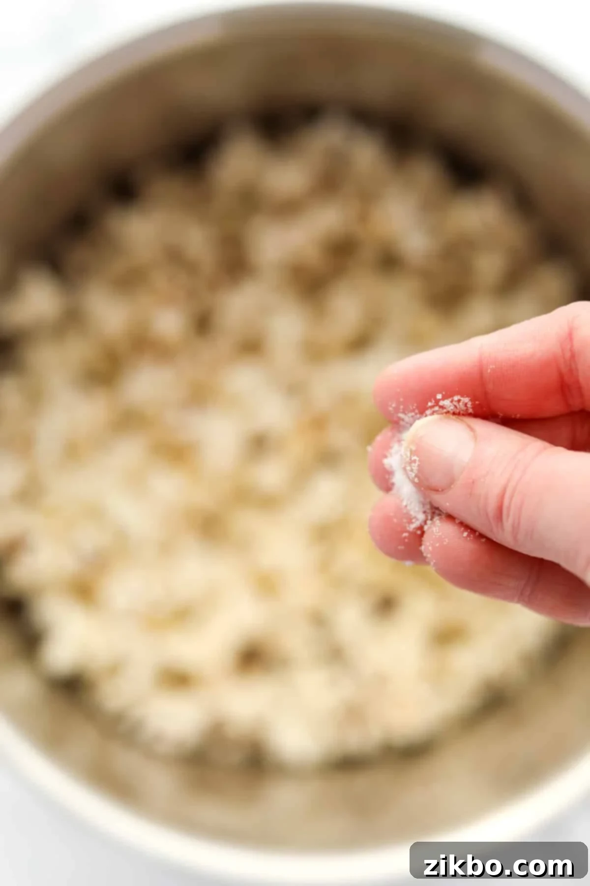 Sprinkling fine salt into a large pot of homemade popcorn, highlighting the seasoning process for optimal flavor.