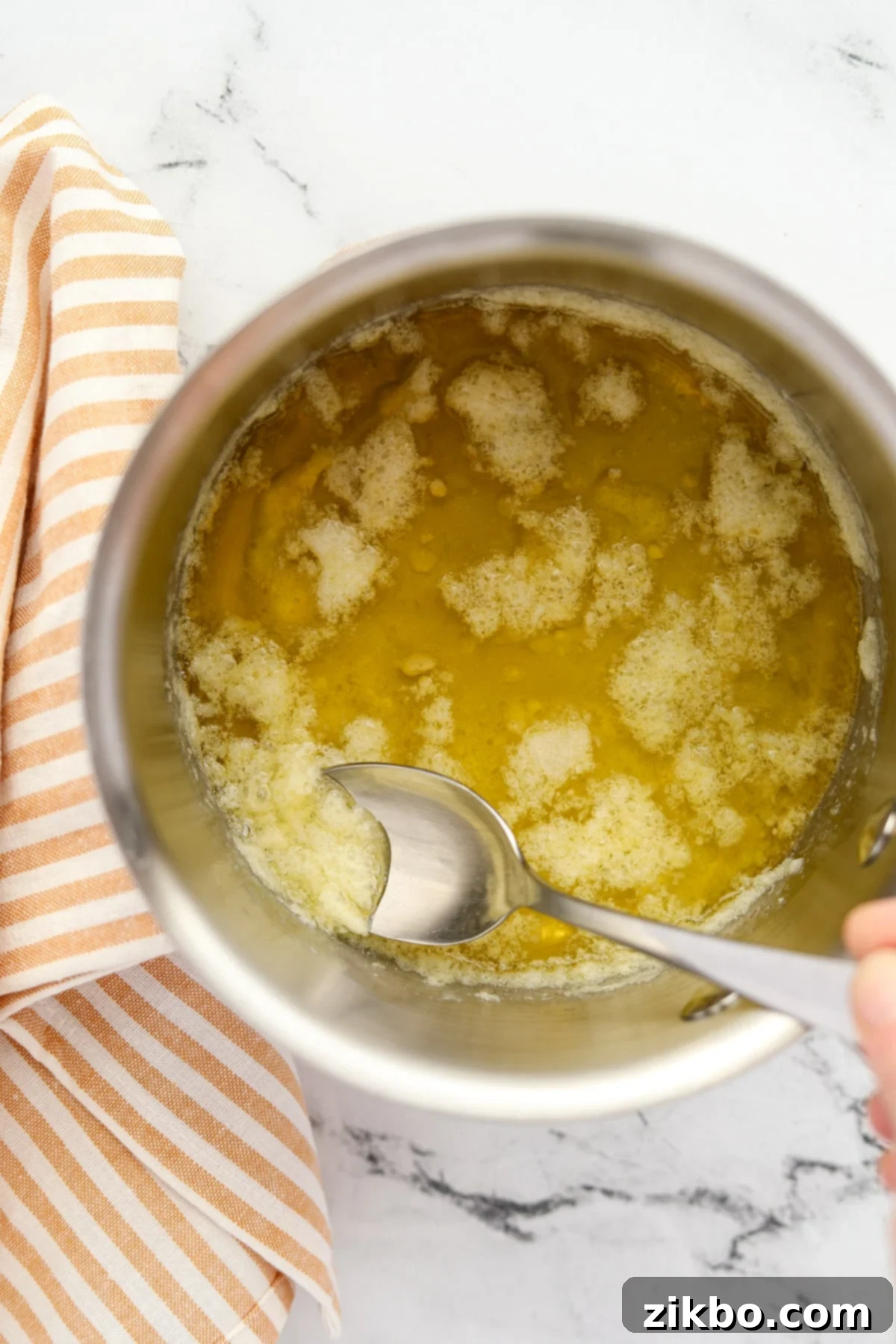 Using a spoon to remove foam from melted butter in a saucepan during the clarification process for popcorn butter.