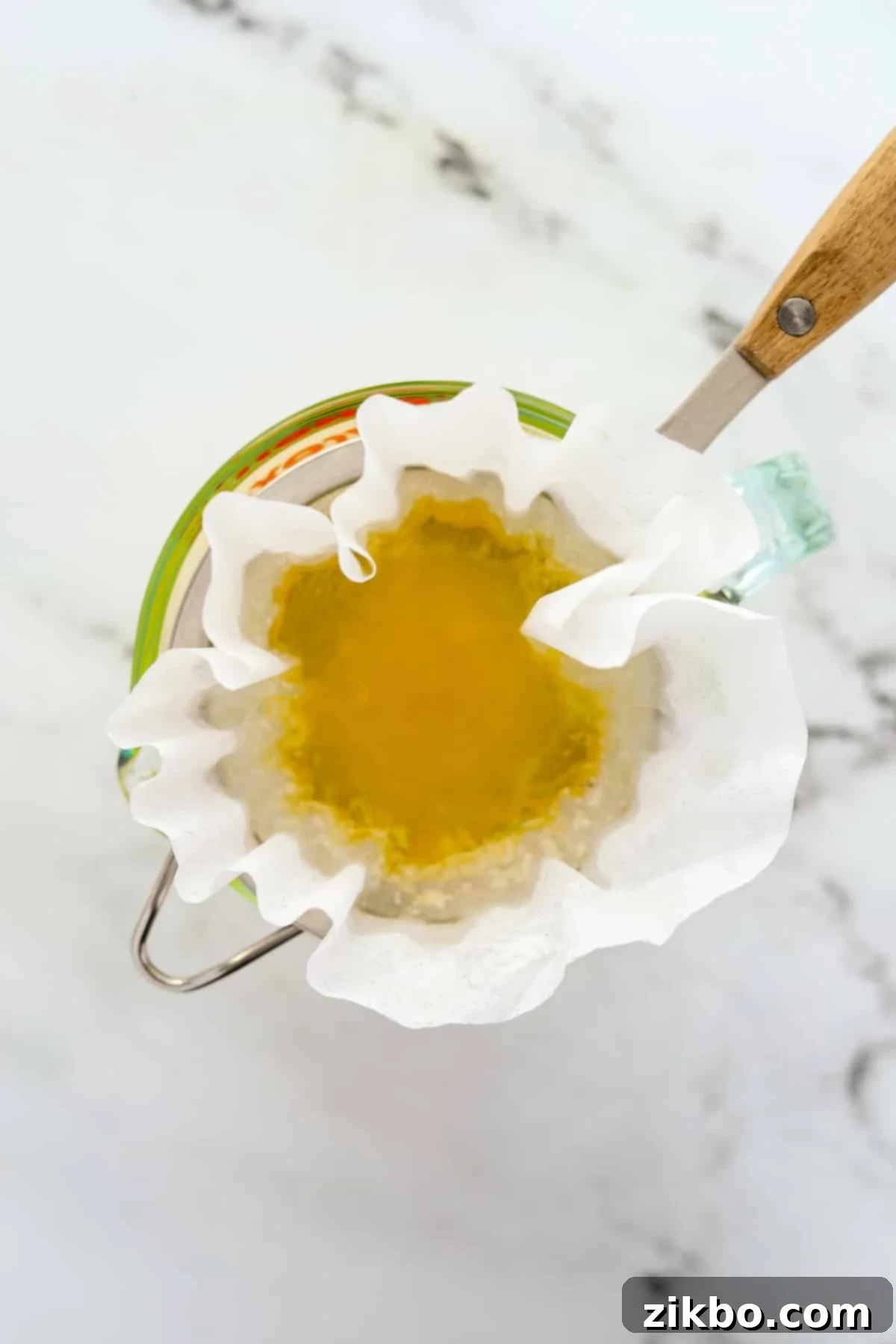 Straining clarified butter through a coffee filter-lined strainer to separate milk solids, creating clear popcorn butter.