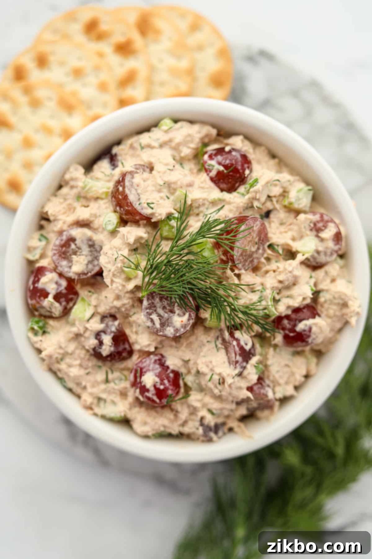A bowl of creamy tuna salad with grapes, garnished with fresh dill.