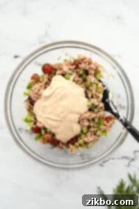 Mixing together tuna salad ingredients with dressing.