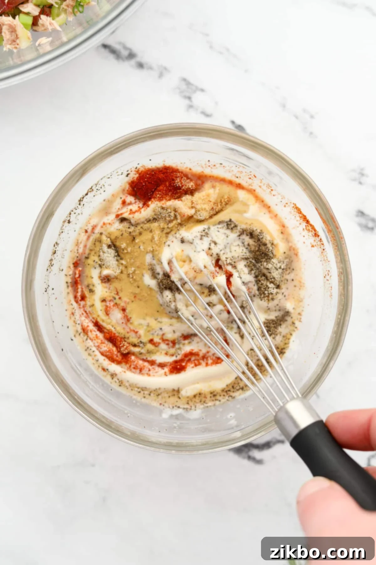 A small bowl with mayonnaise, Dijon mustard, lemon juice, and spices being whisked together to create the creamy dressing for the tuna salad.