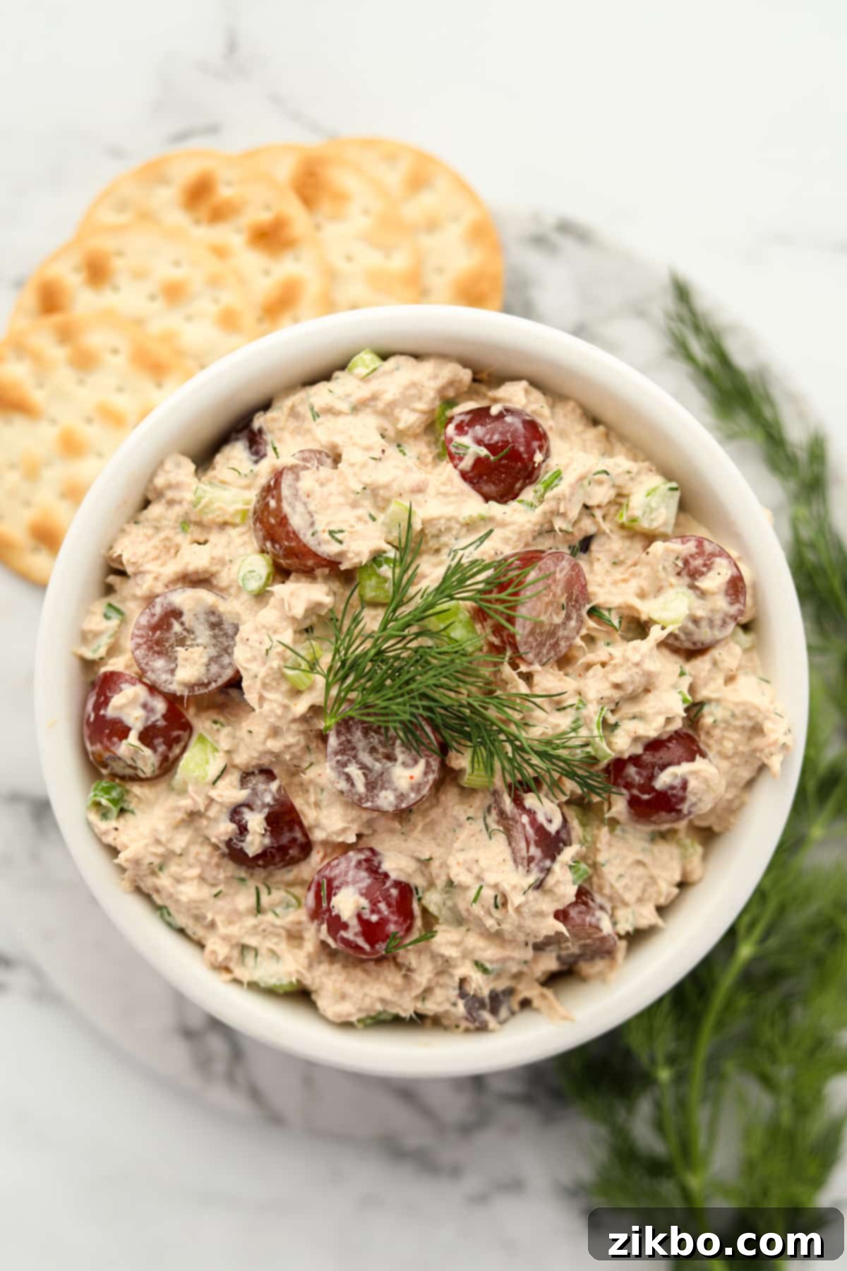 A perfectly mixed bowl of tuna salad with grapes, garnished with fresh dill.