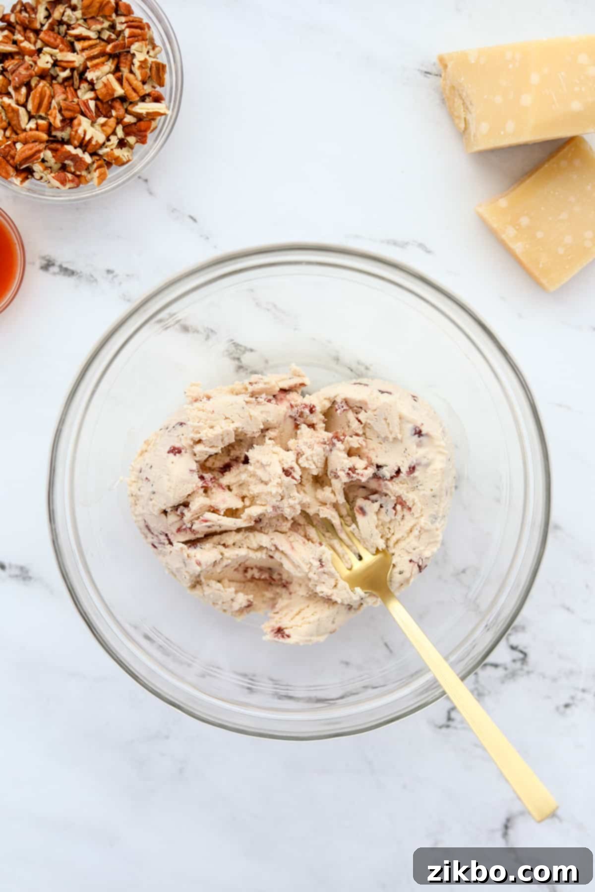 A fork mashing soft Boursin cheese in a white mixing bowl to achieve a smooth consistency.