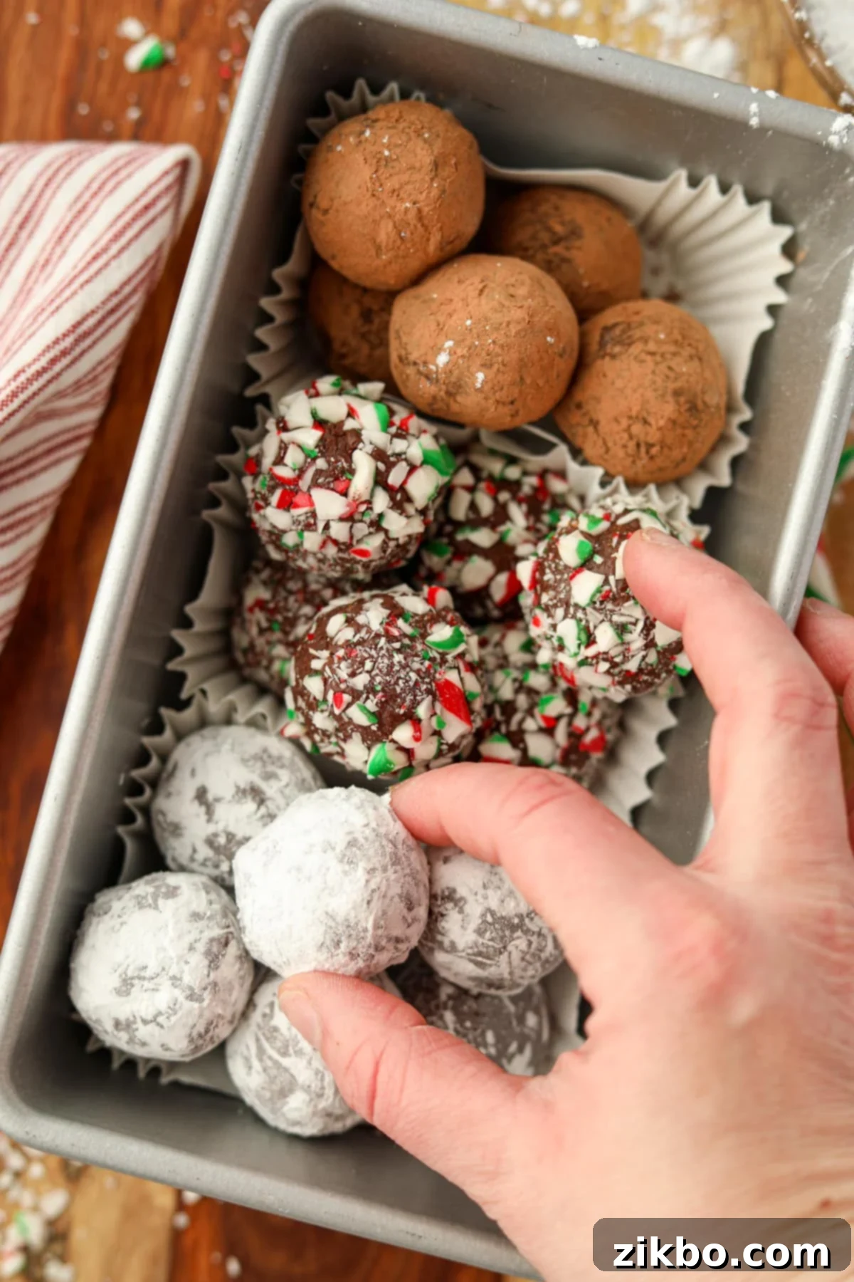 A hand taking a powdered sugar coated chocolate ball from a container.