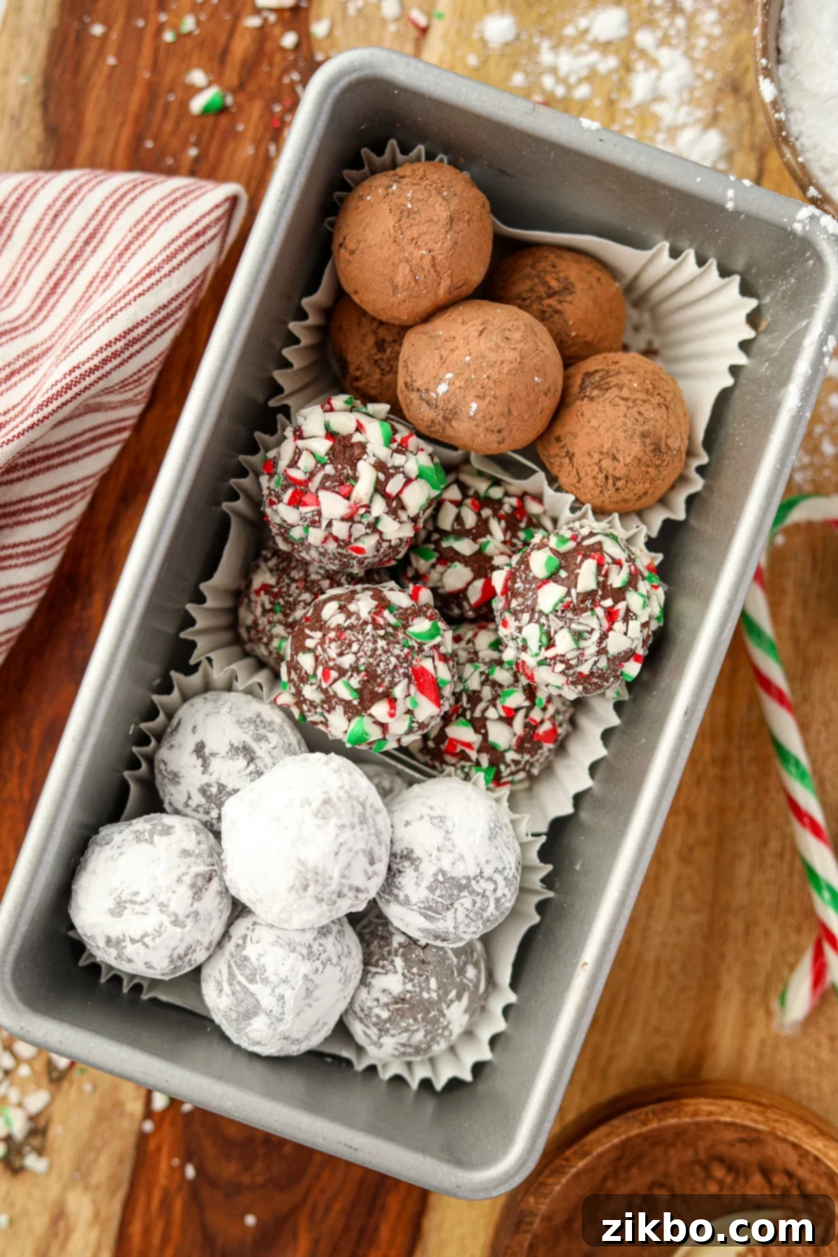 A metal loaf pan filled with homemade truffles; one coated with cocoa powder, another with crushed candy canes, and a third with powdered sugar.