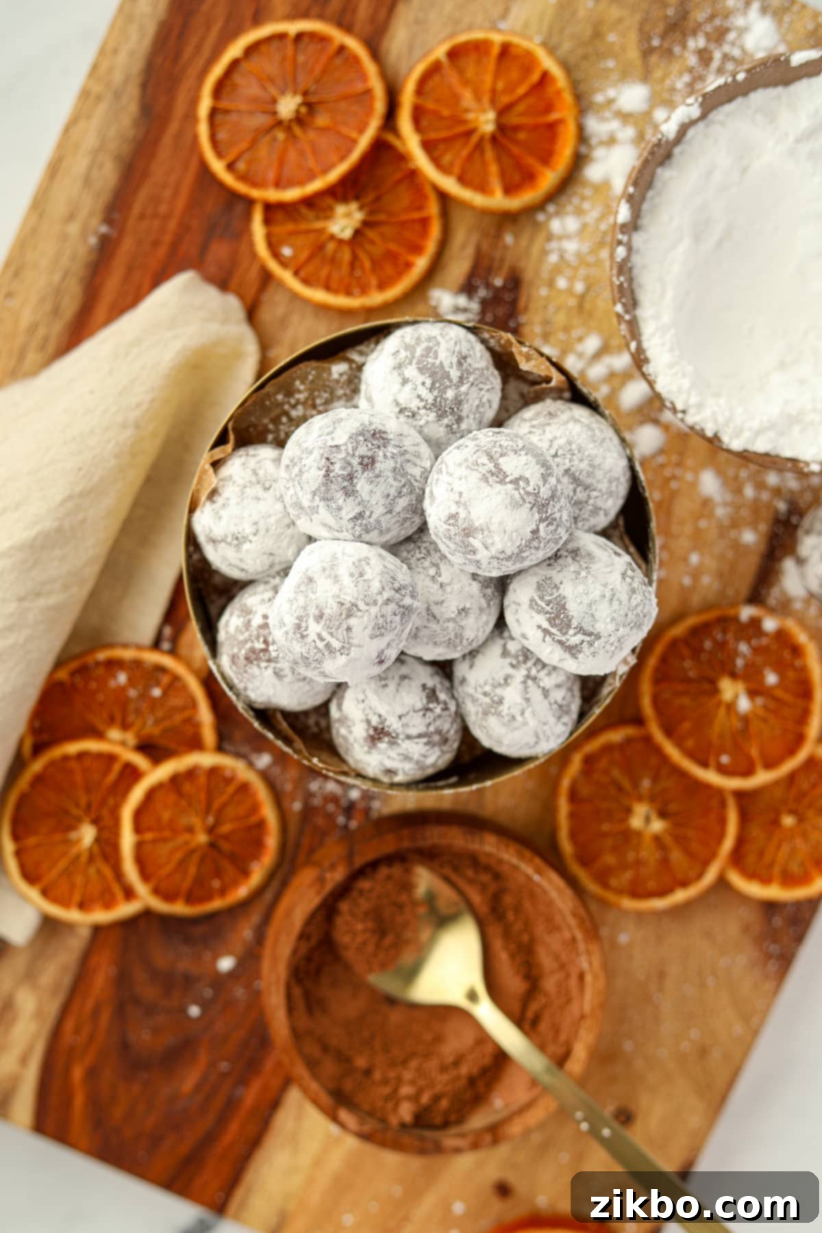 A bowl of chocolate orange truffles coated in powdered sugar, beautifully presented with dried orange slices scattered around them.