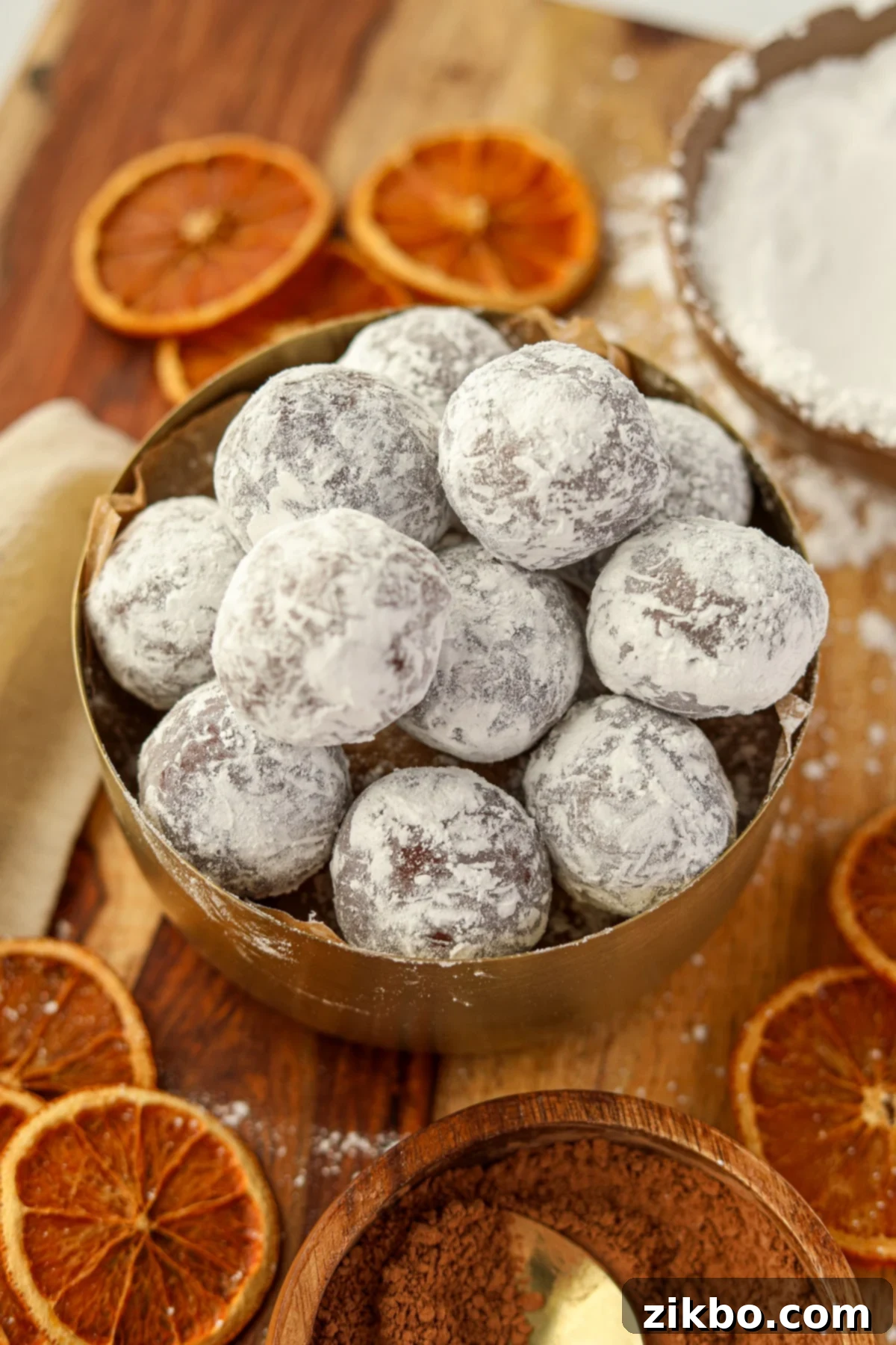 Close-up of chocolate balls coated in powdered sugar, with a subtle background of dried orange slices on a rustic counter.