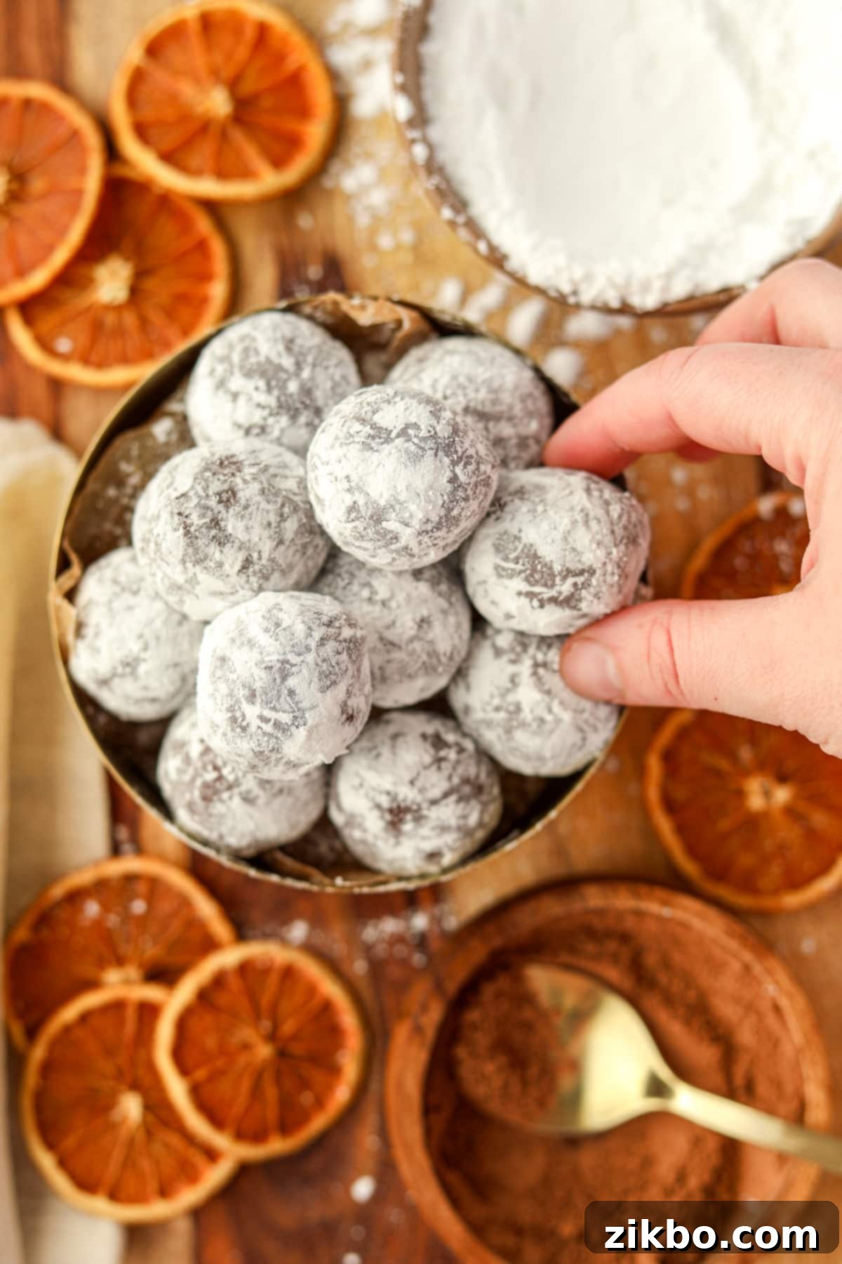 A hand reaching into a bowl to pick a chocolate orange truffle, highlighting its tempting appearance.
