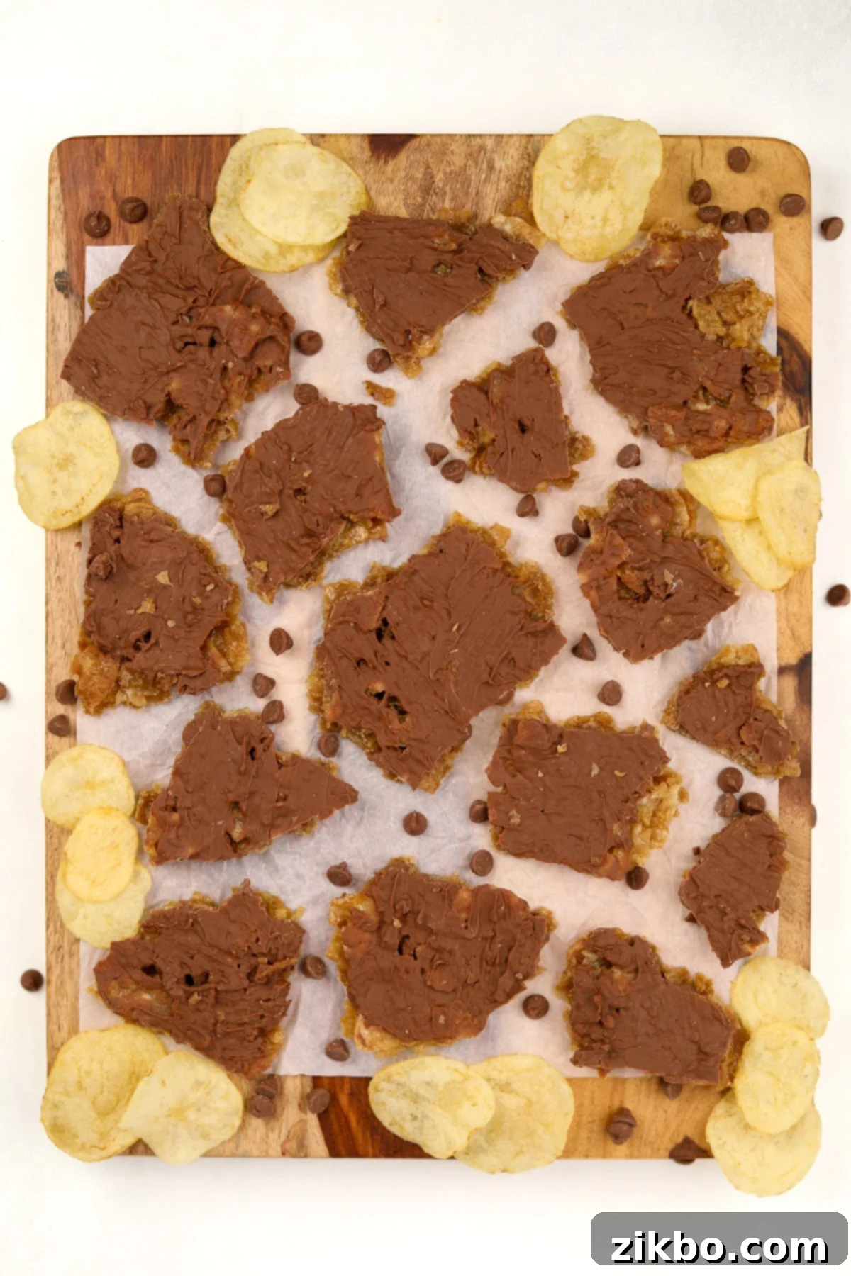 Various irregular pieces of homemade chocolate potato chip toffee scattered on a wooden cutting board, highlighting the distinct layers and crunchy texture.
