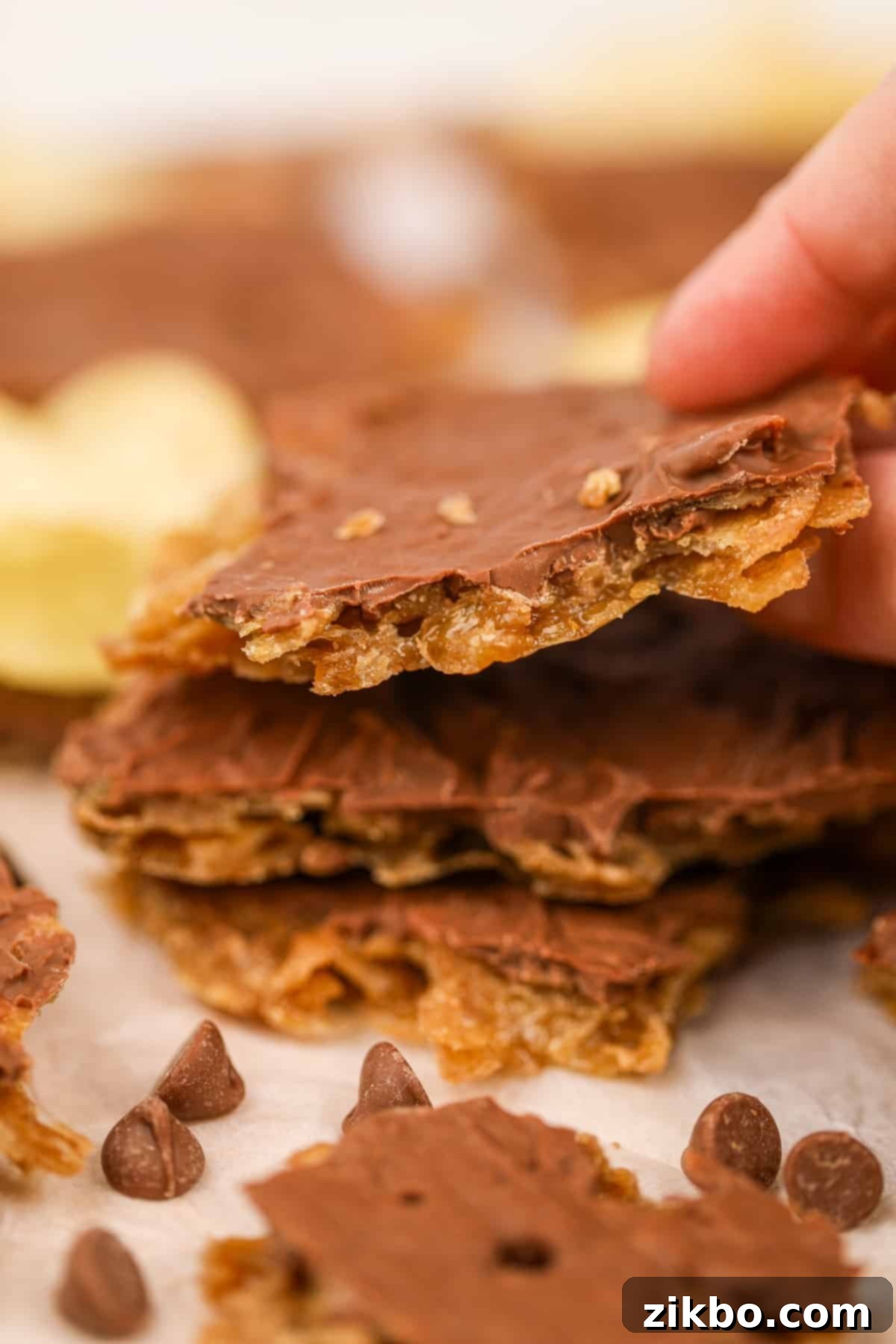 A close-up shot of a single piece of homemade potato chip toffee, featuring the thin, smooth layer of melted chocolate on top, and the visible crunch of the toffee and chips below.