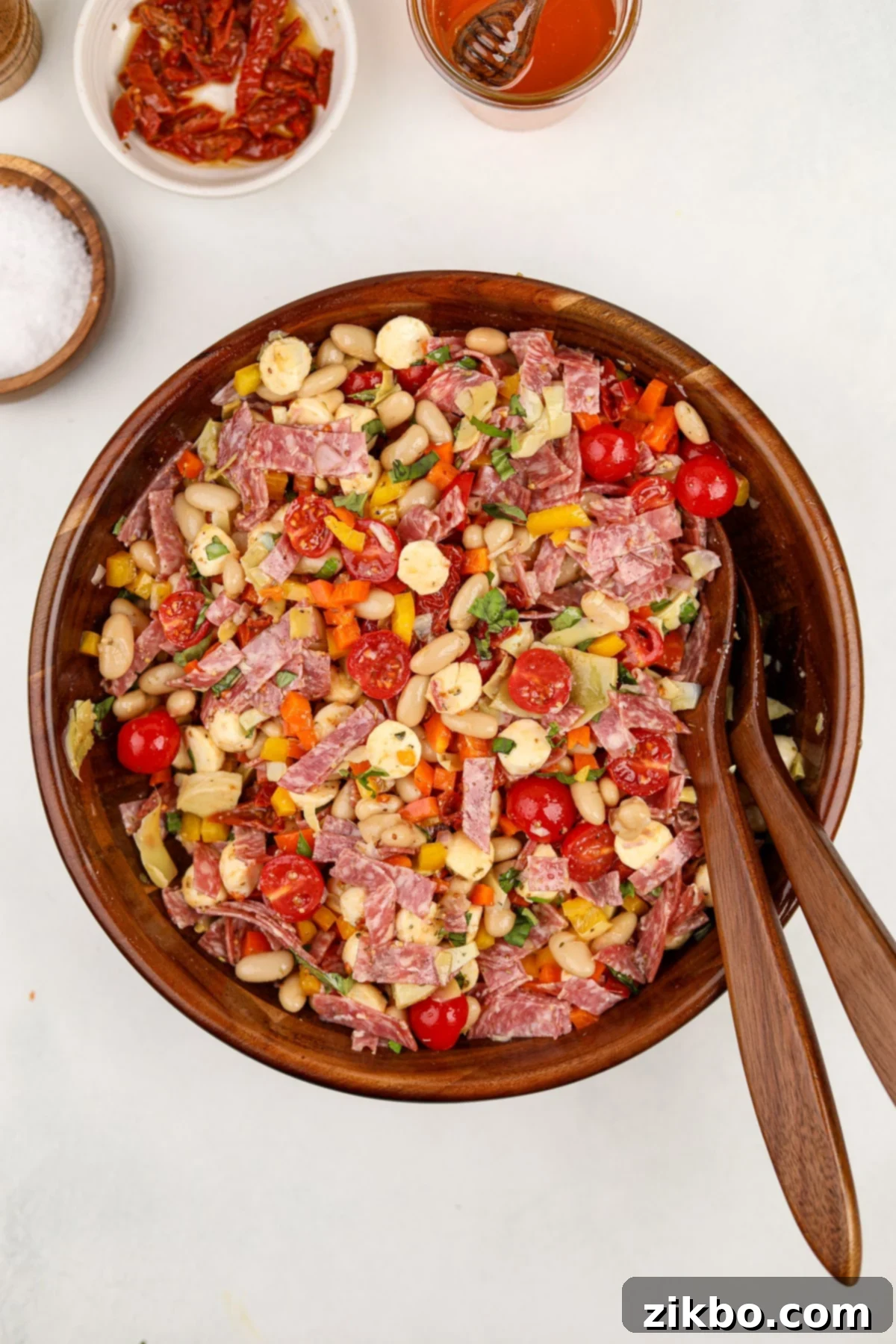 Classic Italian Bean Salad 5 A salad bowl filled with salad featuring white beans, cherry tomatoes, salami, and mini mozzarella balls.