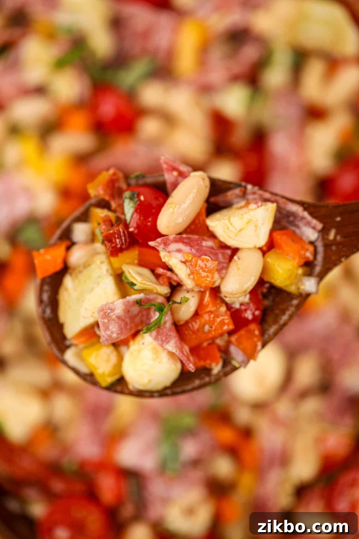 Classic Italian Bean Salad 8 A wooden spoon holding up a small portion of white bean salad with salami and sun-dried tomatoes.