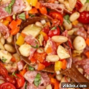 Classic Italian Bean Salad 9 A wooden spoon scooping a portion of bean salad with sun-dried tomatoes, mozzarella, and basil.