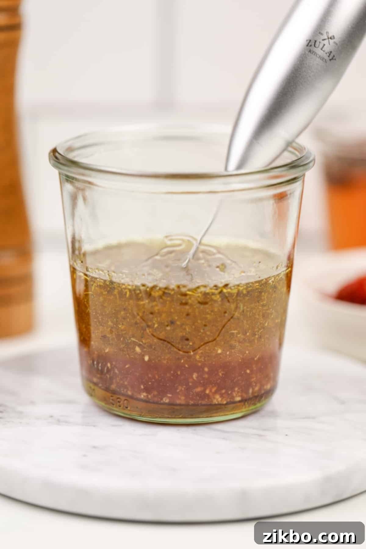 A glass jar with layers o of oil and vinegar, with a small frother want sticking out of the side.