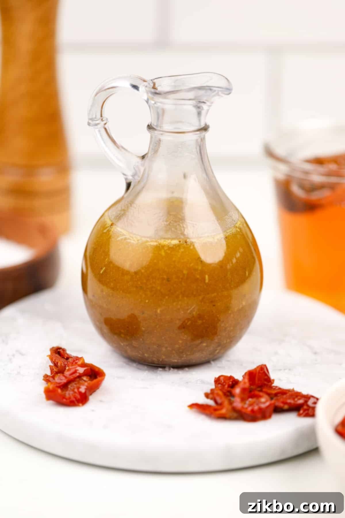 A cruet filled with homemade dressing; sundried tomatoes on the marble around it.