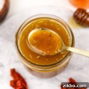 A small jar filled with homemade vinaigrette, a golden spoon taking a small amount.