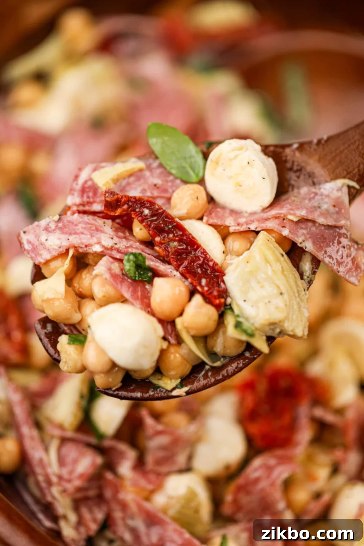 A wooden spoon full of bean salad featuring sun-dried tomatoes, mozzarella, and fresh basil.
