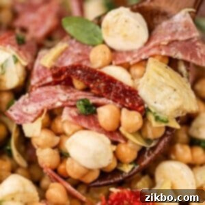 A wooden spoon scooping bean salad made with mozzarella, sun-dried tomato, and basil.