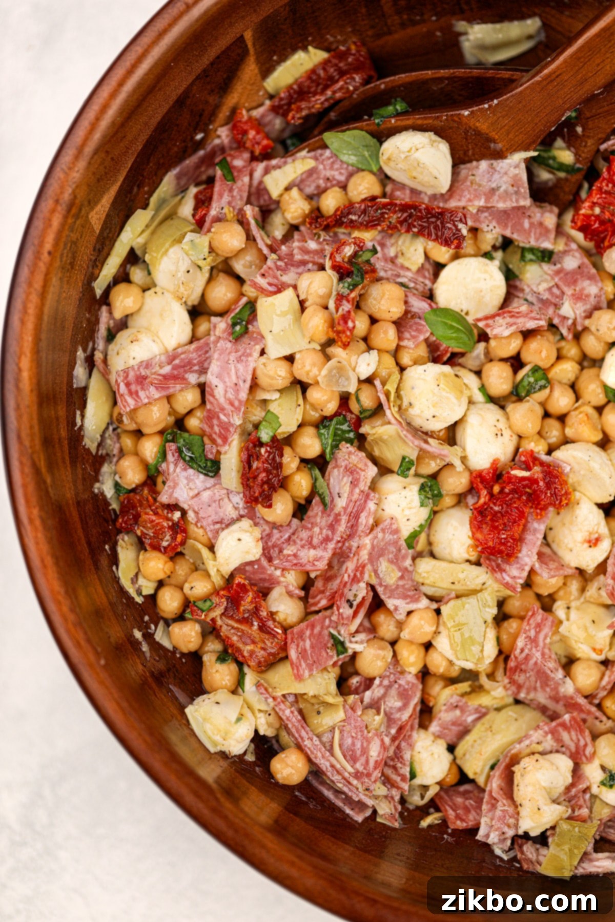 A wooden salad bowl filled with a chickpea and salami bean salad.