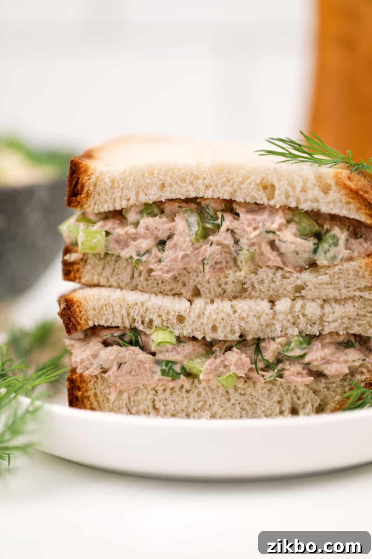 Bright Dill Tuna Salad 2 A stack of delicious tuna sandwiches on a white plate, garnished with fresh dill.