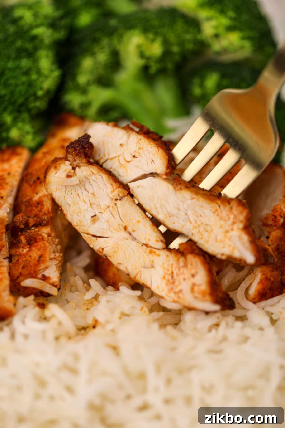 Two strips of chicken speared onto a gold fork.