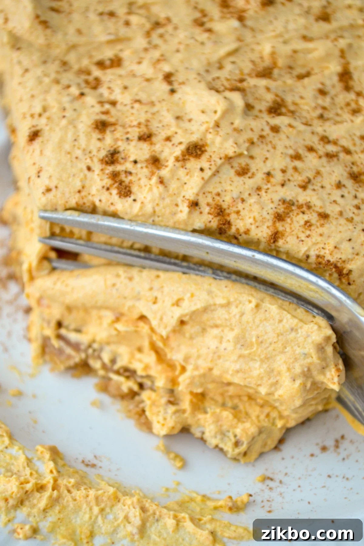 A beautiful piece of pumpkin fluff pie, with a fork poised to take a bite, highlighting the delightful layers.