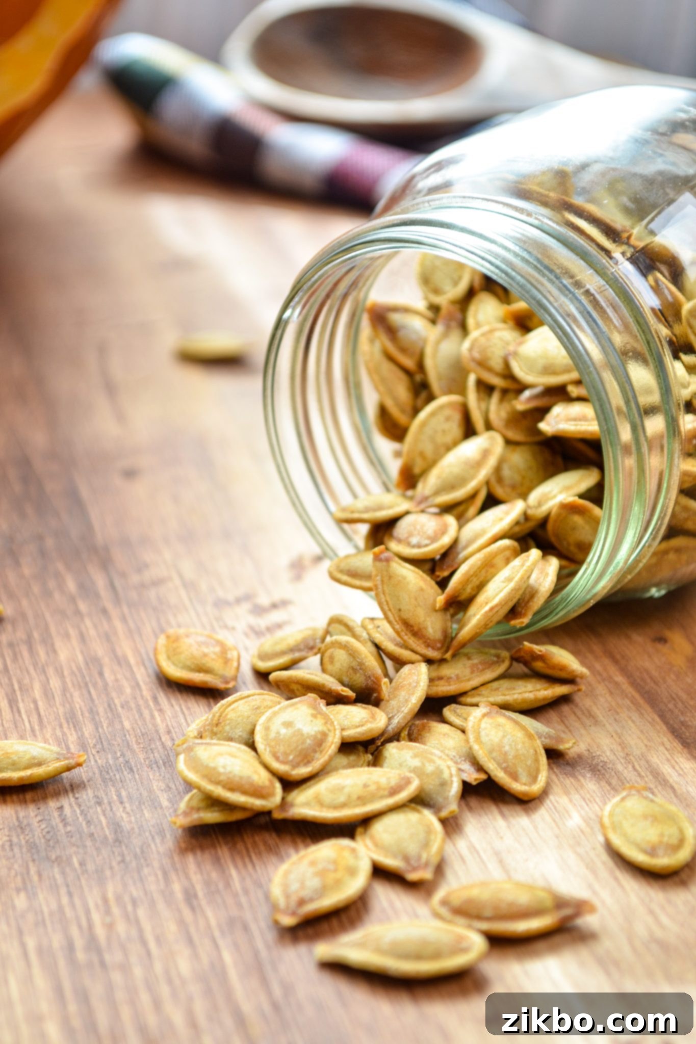 A jar of pumpkin seeds spilling onto a wood table, evoking a rustic fall aesthetic.