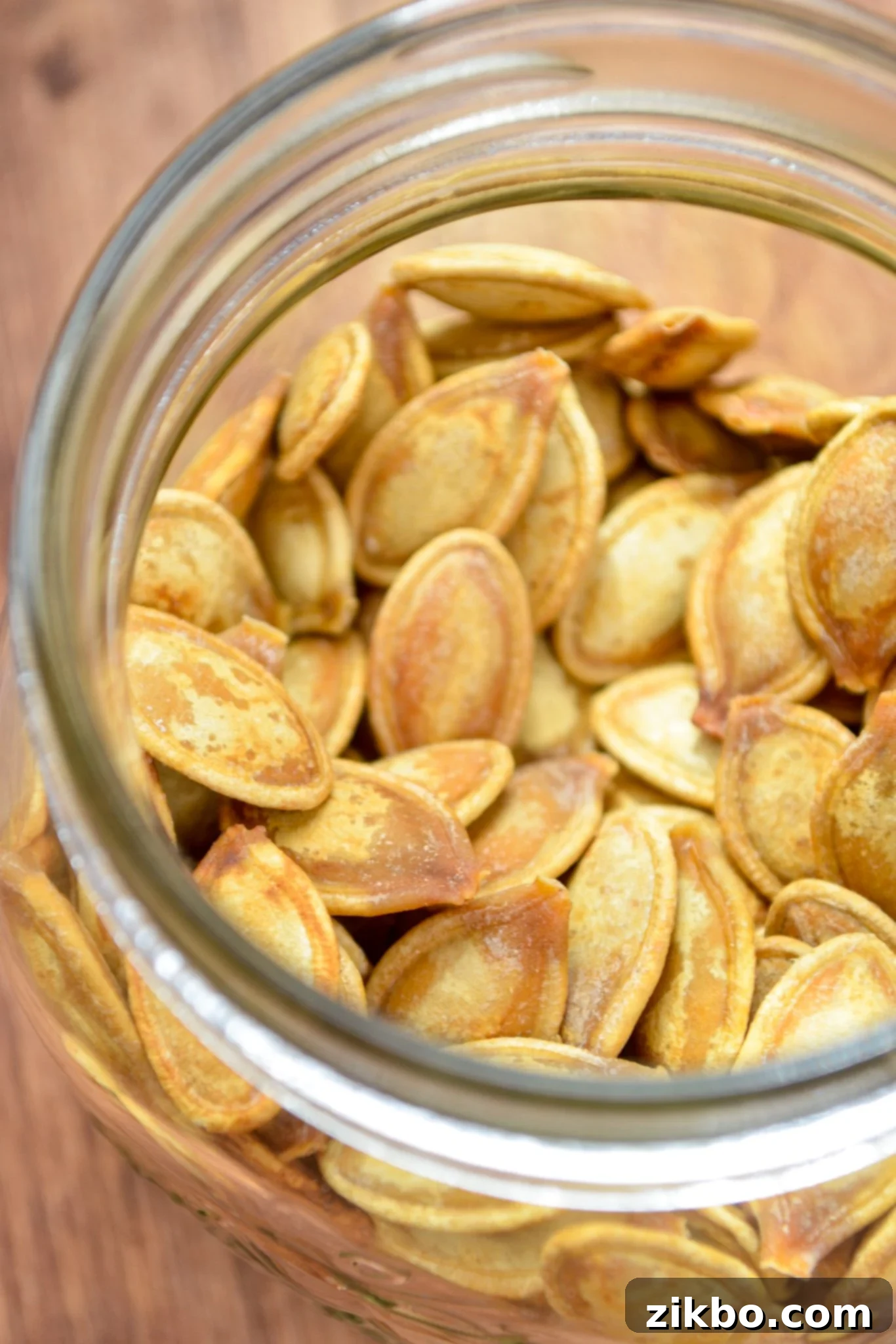 A beautifully clear glass jar filled to the brim with golden, crispy roasted pumpkin seeds.