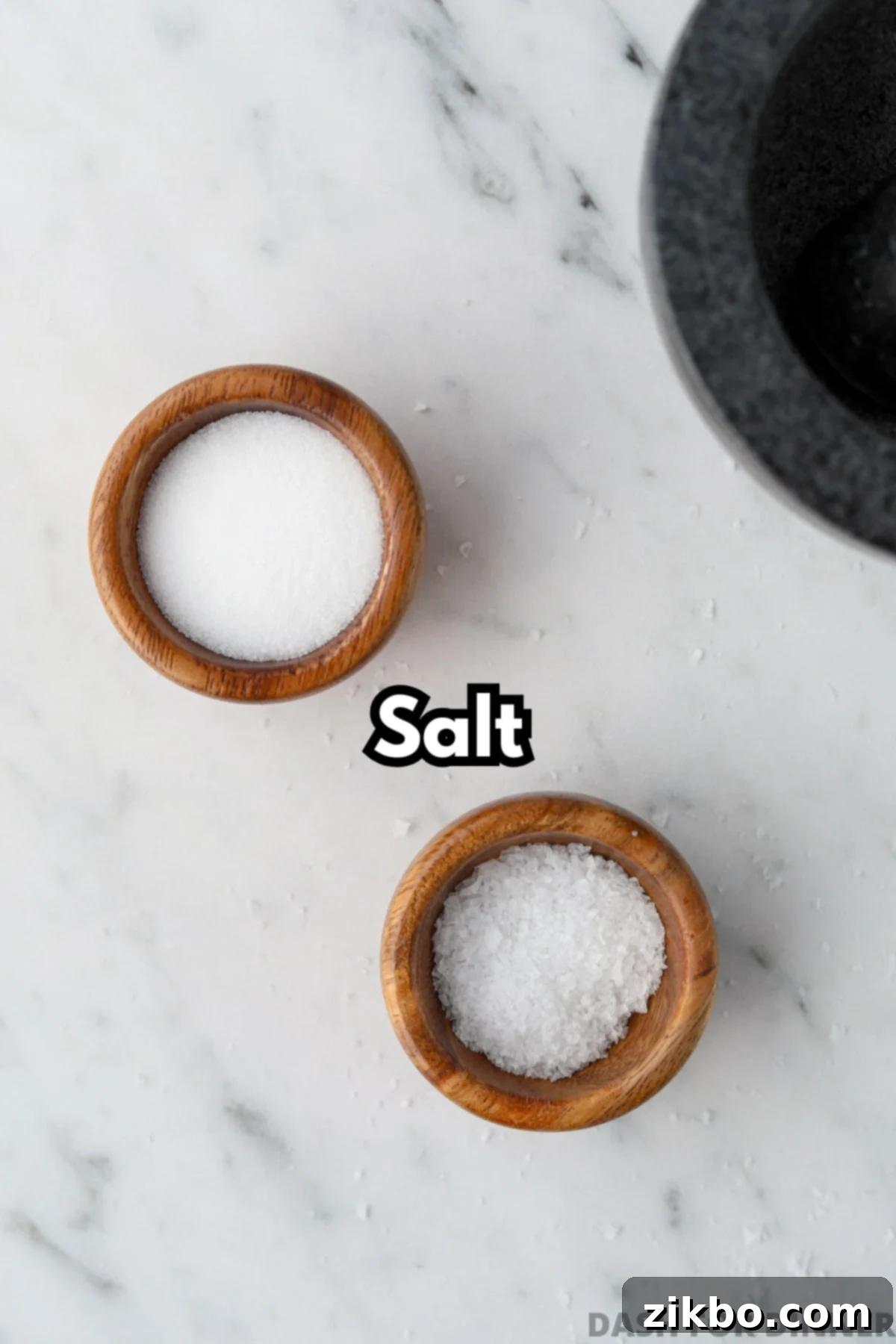 Two small wooden bowls filled with both fine salt and flaky salt.