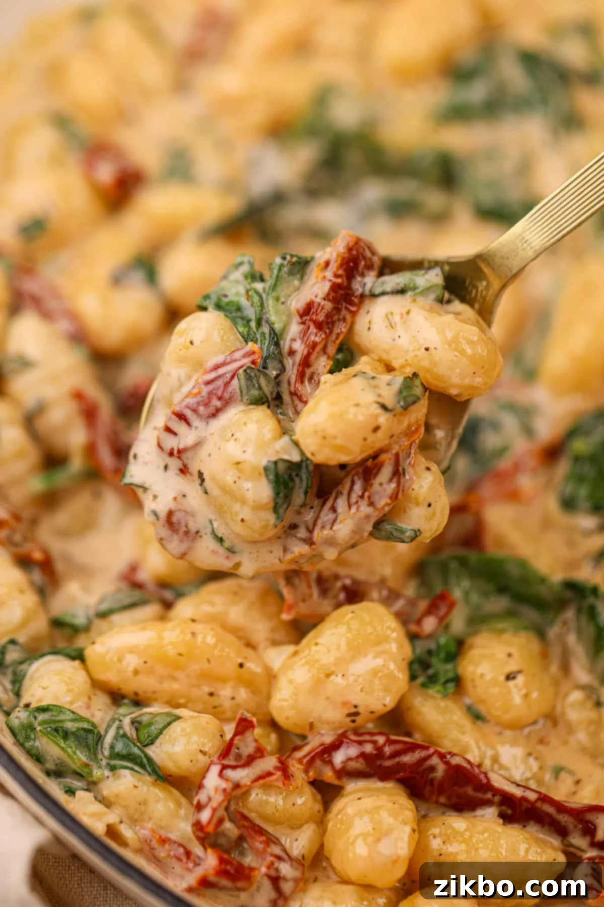 A spoon taking a portion of creamy gnocchi from a large pile, highlighting its rich texture and vibrant ingredients.