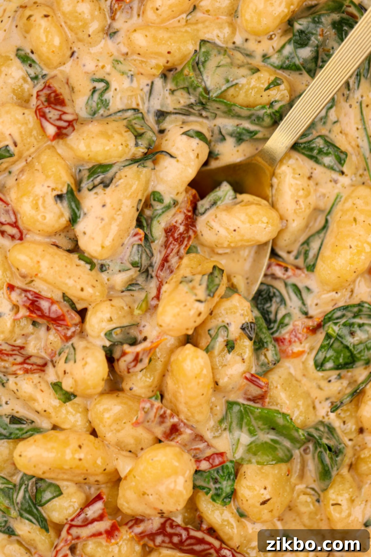 A large spoon taking a generous portion of creamy gnocchi from a pan, showing the delightful texture and ingredients.