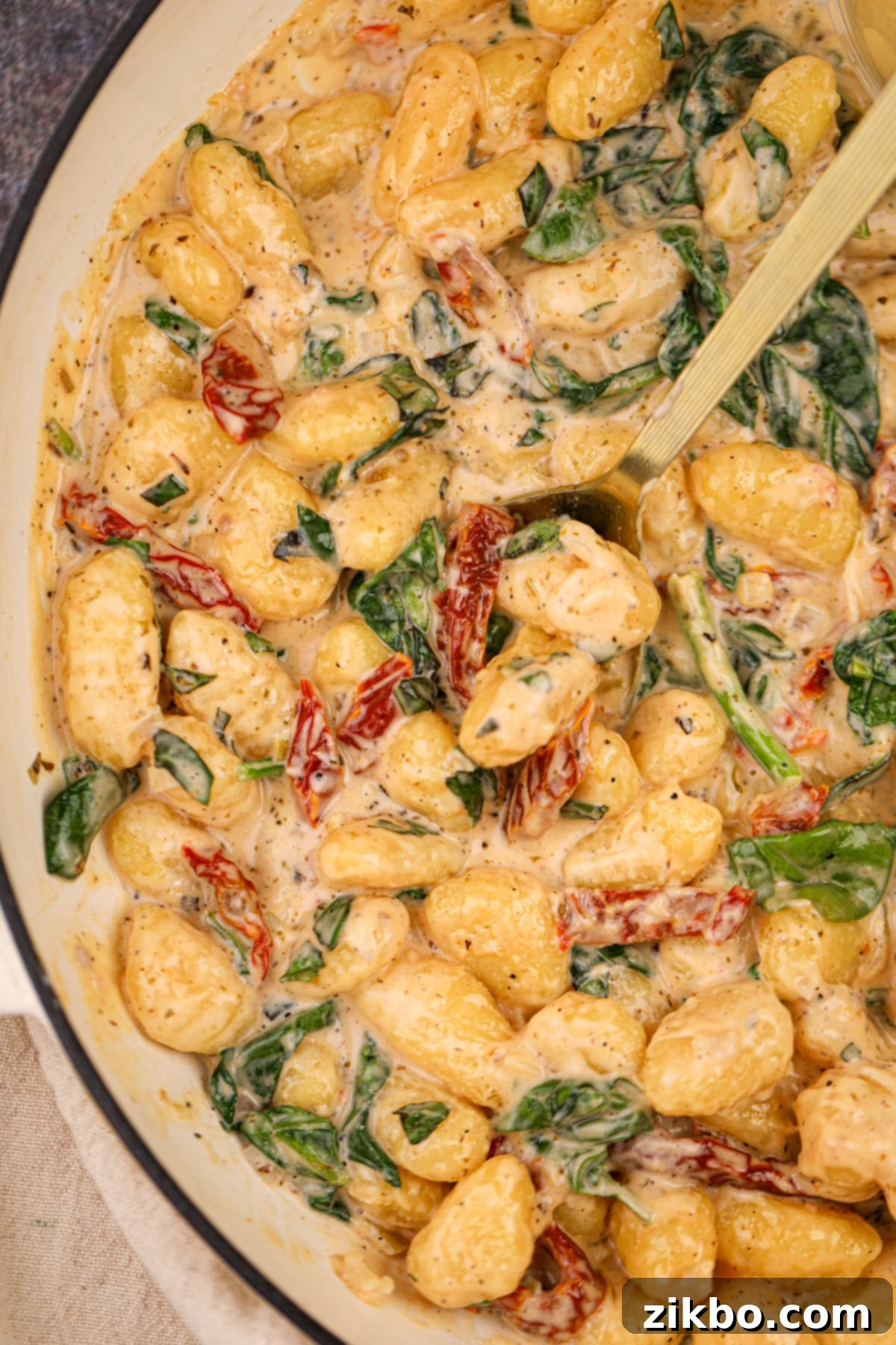 A large skilled filled with creamy gnocchi, with a spoon sticking out, inviting another serving.