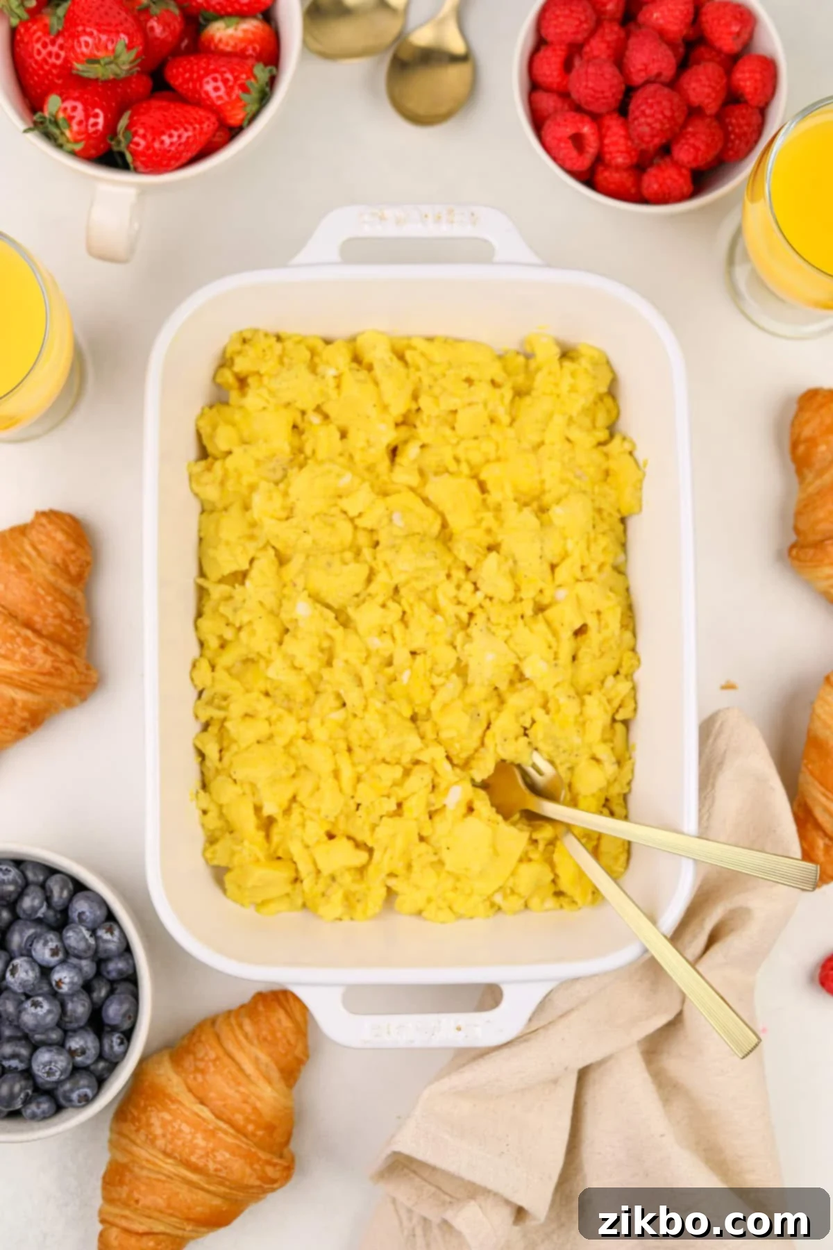 A white baking dish filled with cooked eggs, surrounded by fresh berries.