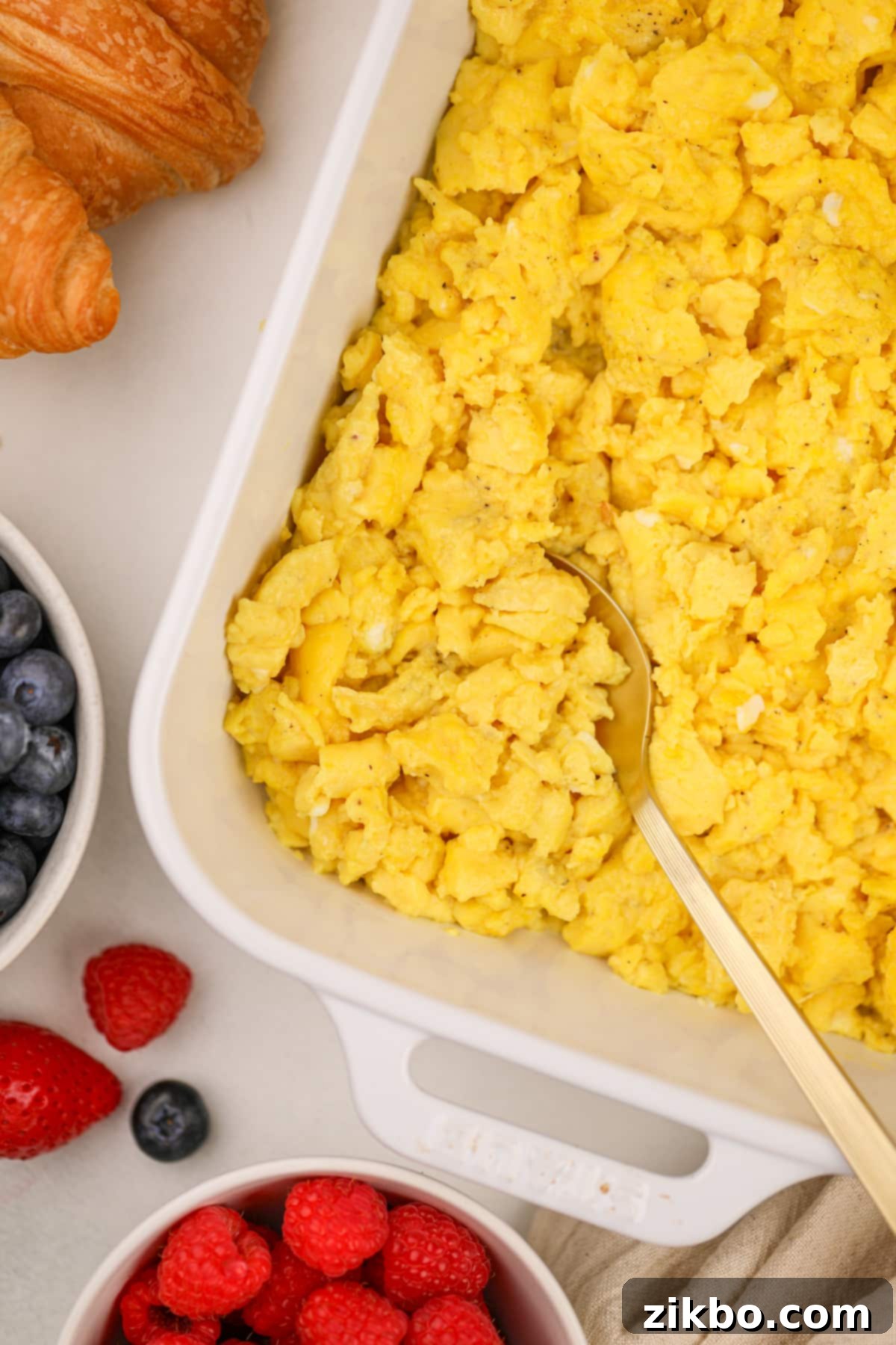 A gold spoon scooping scrambled eggs from a baking dish.